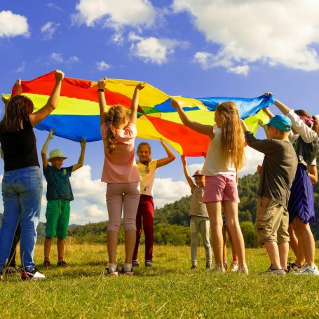 Children playing with a large, colourful parachute on a sunny day outdoors.